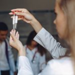 A woman holds a syringe, standing before a group of attentive doctors in a clinical setting